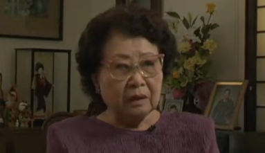 Barbara Kawakami still from video interview, framed pictures and flowers in the background